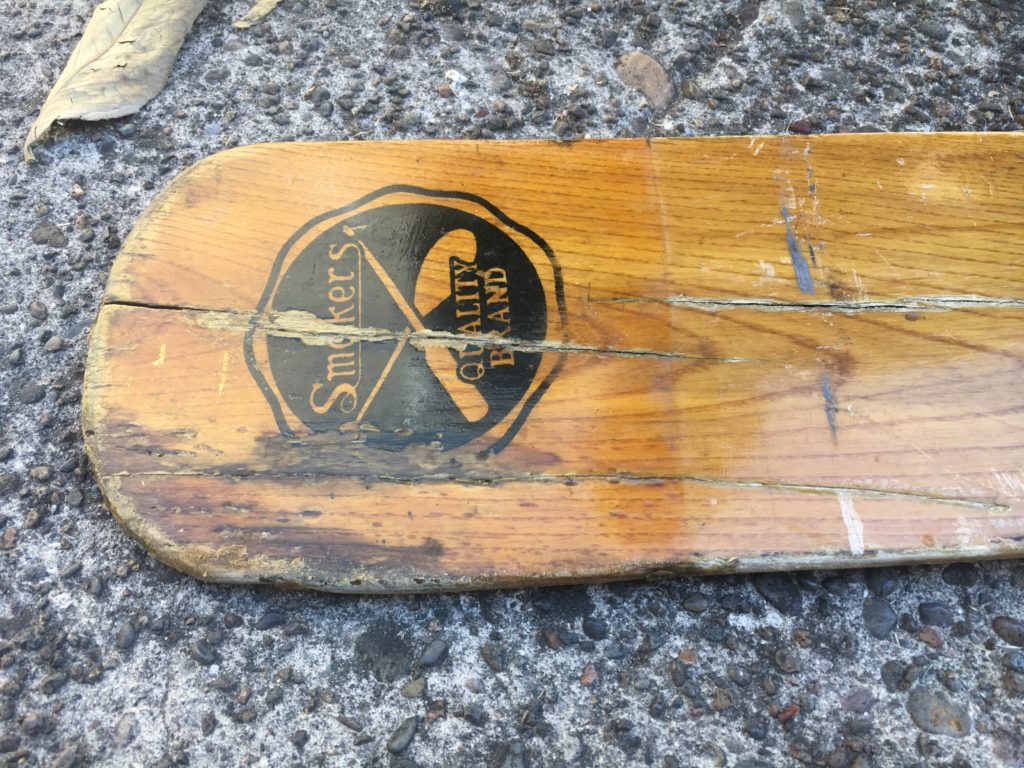 The tip of a Smokers brand oar made of ash. It has rot, cracks, and even two wood screws in it.